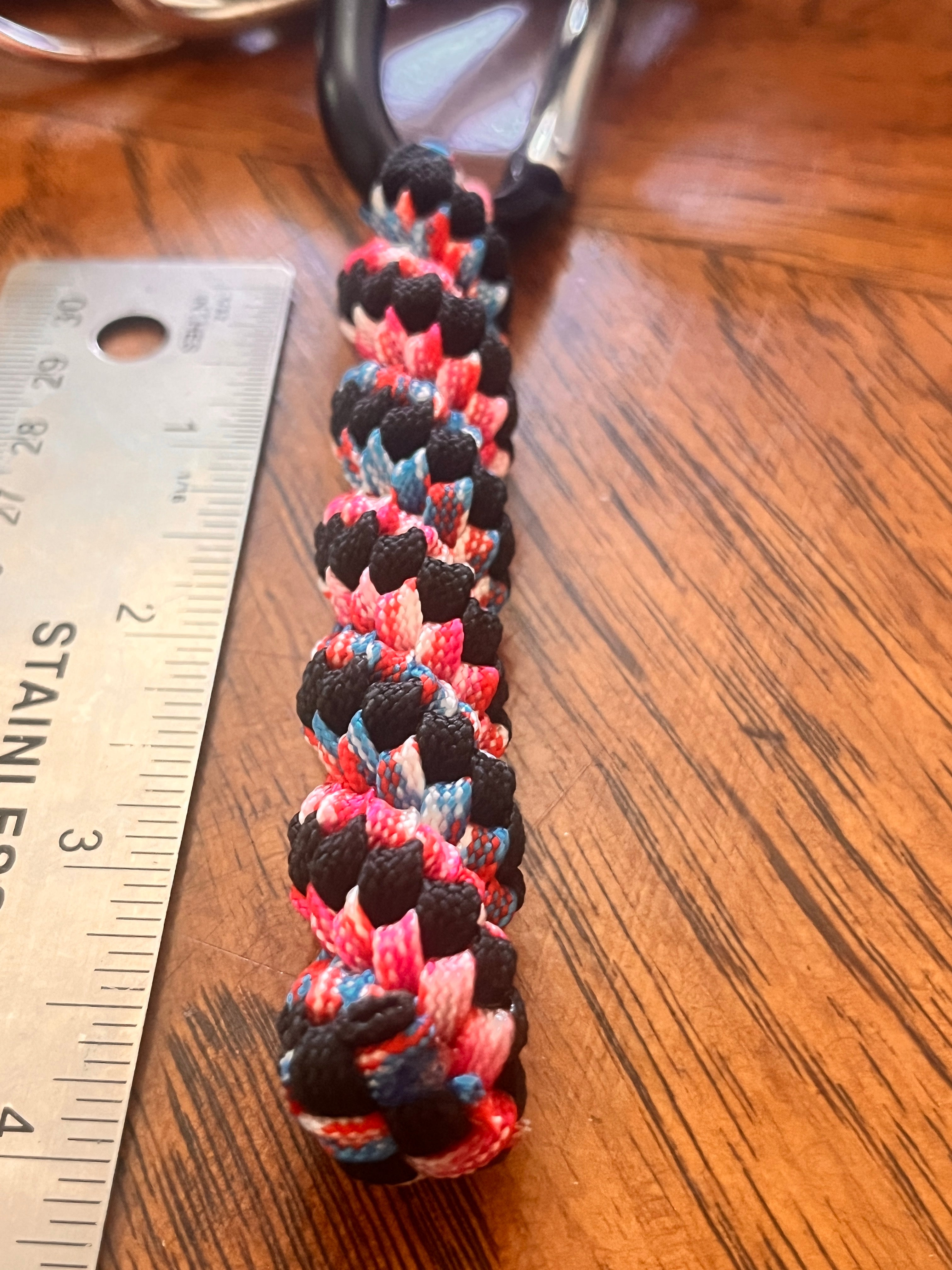Multicolored braided cord on a wooden surface with a ruler for scale.